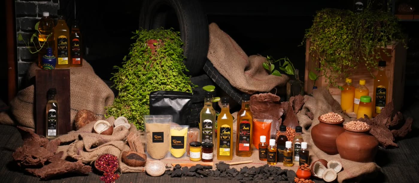 The Anshi range photographed together: oil bottles with black labels, clear pouches of powder and grain, small jars, on hessian.