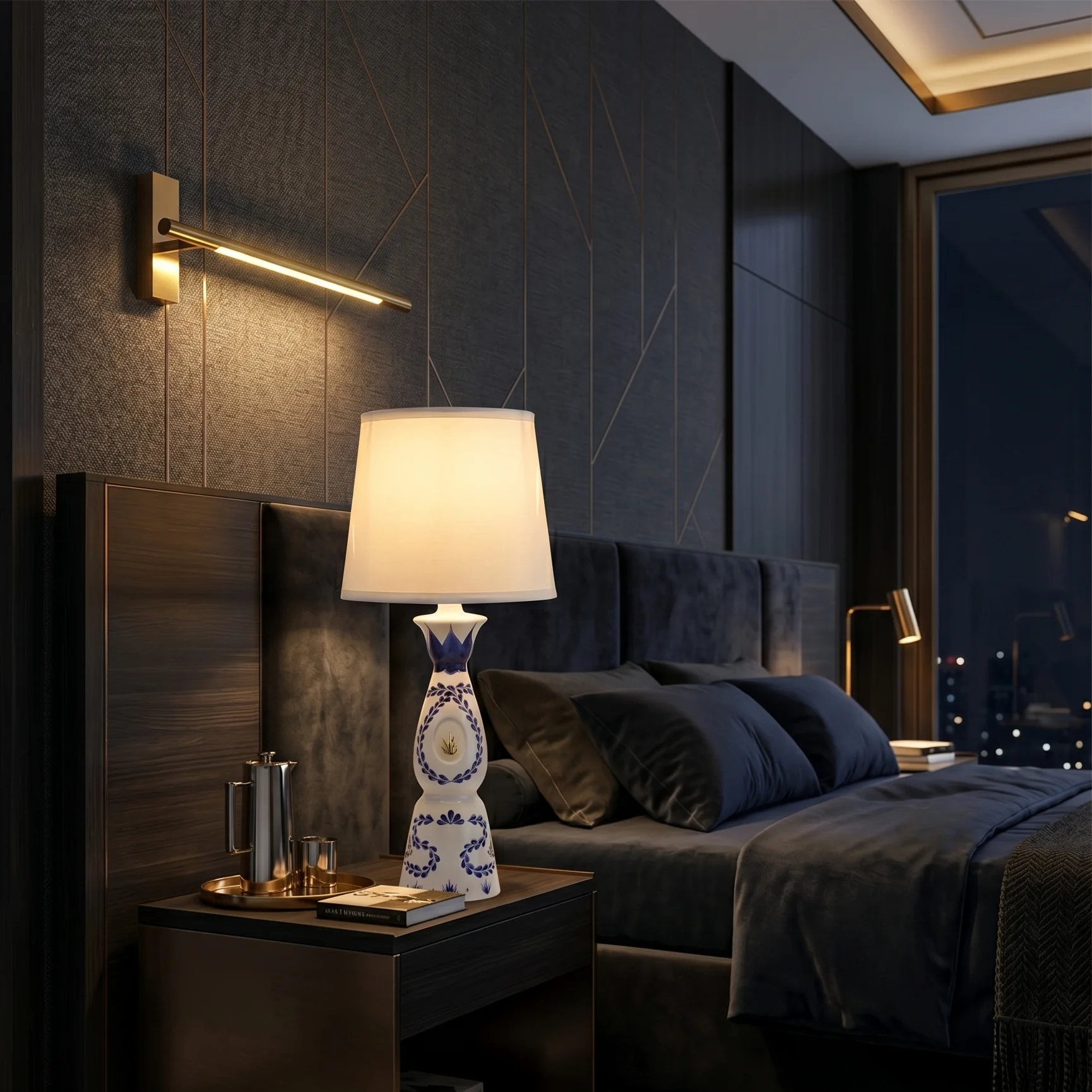 The lamp lit on a bedside table, a dark upholstered bed and a night skyline through the window.